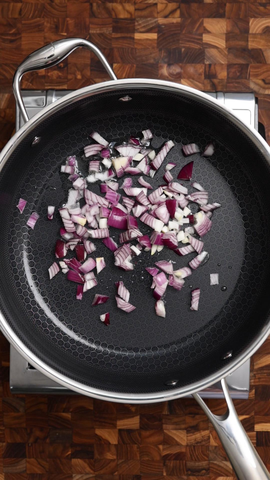Chopped red onion added to the hot oil in a pan.