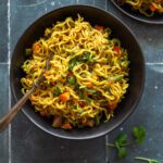 Masala maggi noodles served in two black ceramic bowls, garnished with chopped coriander on top.