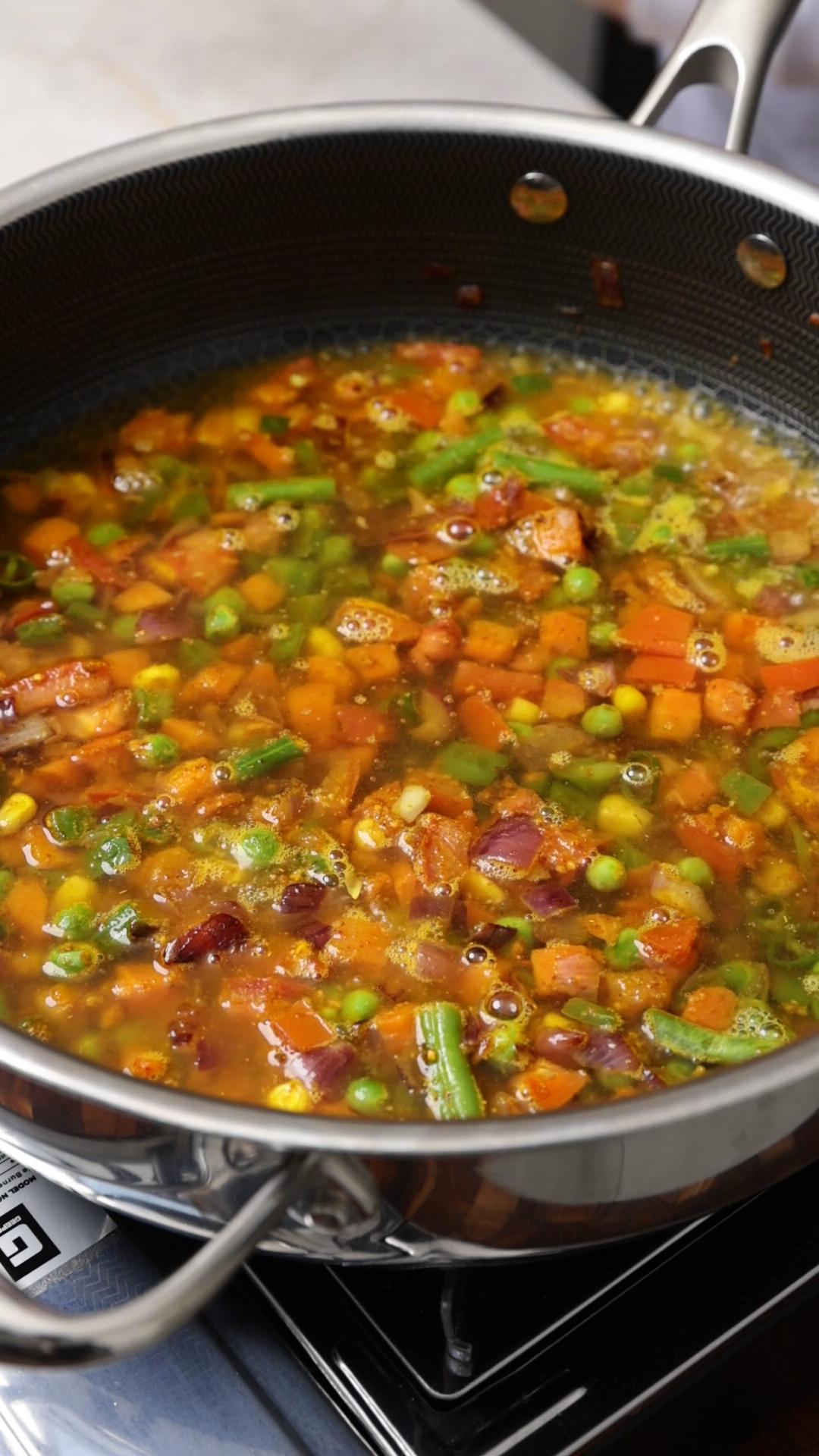 Boiling water added to the spiced mixed vegetables in a pan.