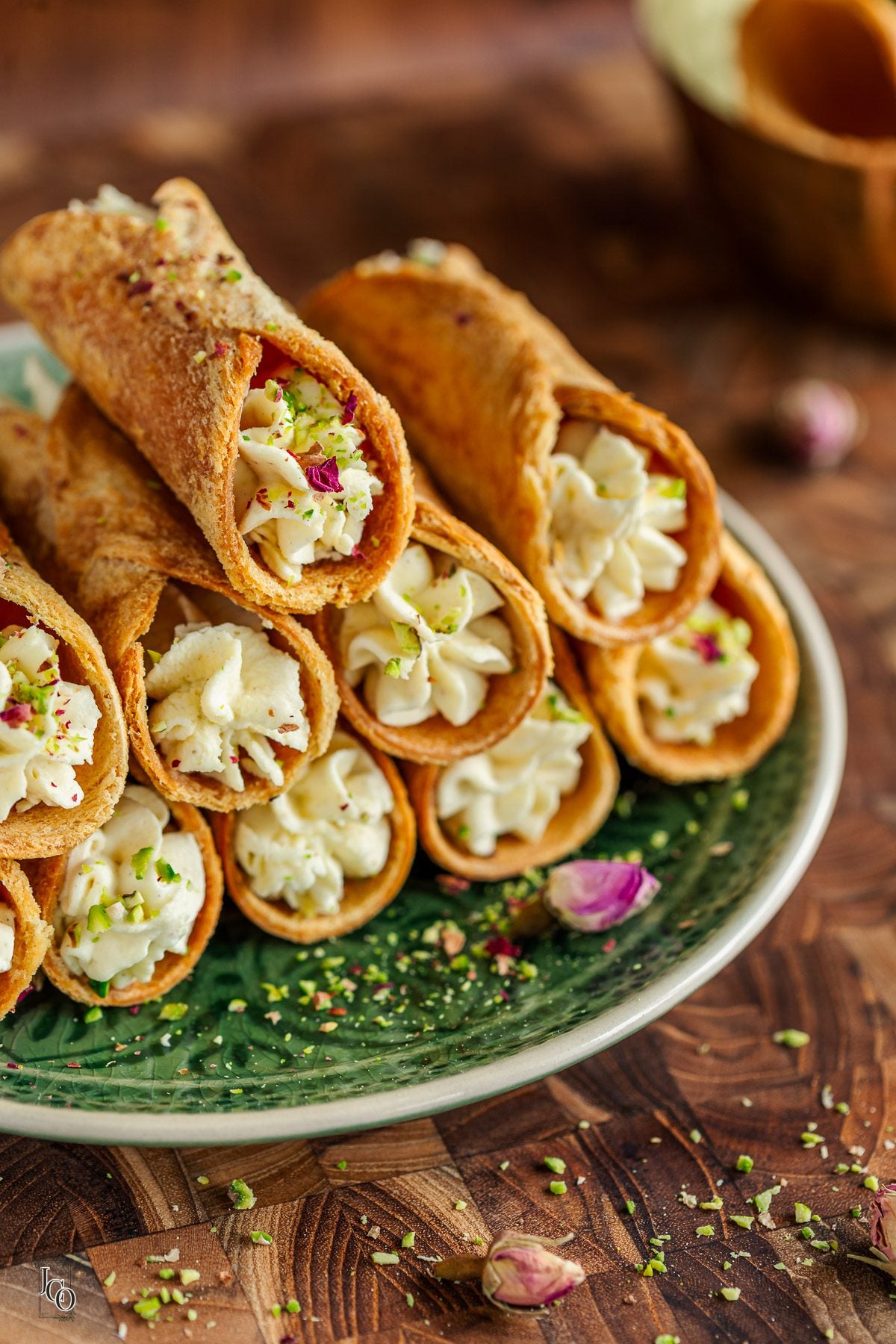 A stack of cream filled cannoli on a round plate, garnished with rose petals and pistachio.