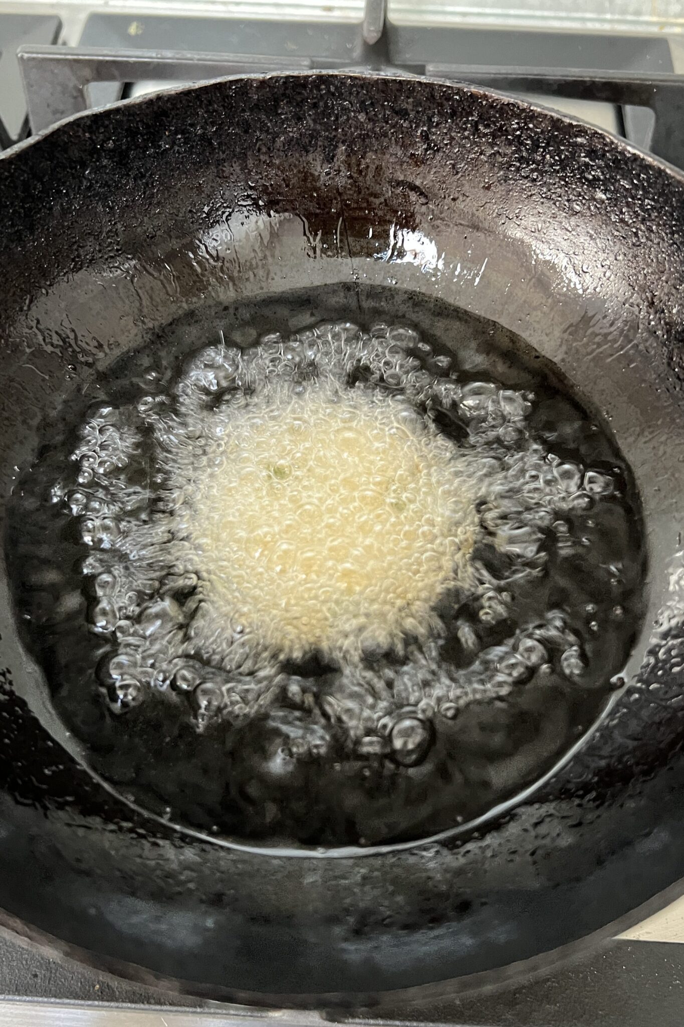 One uncooked chana dal vada added to the hot oil in a kadai.