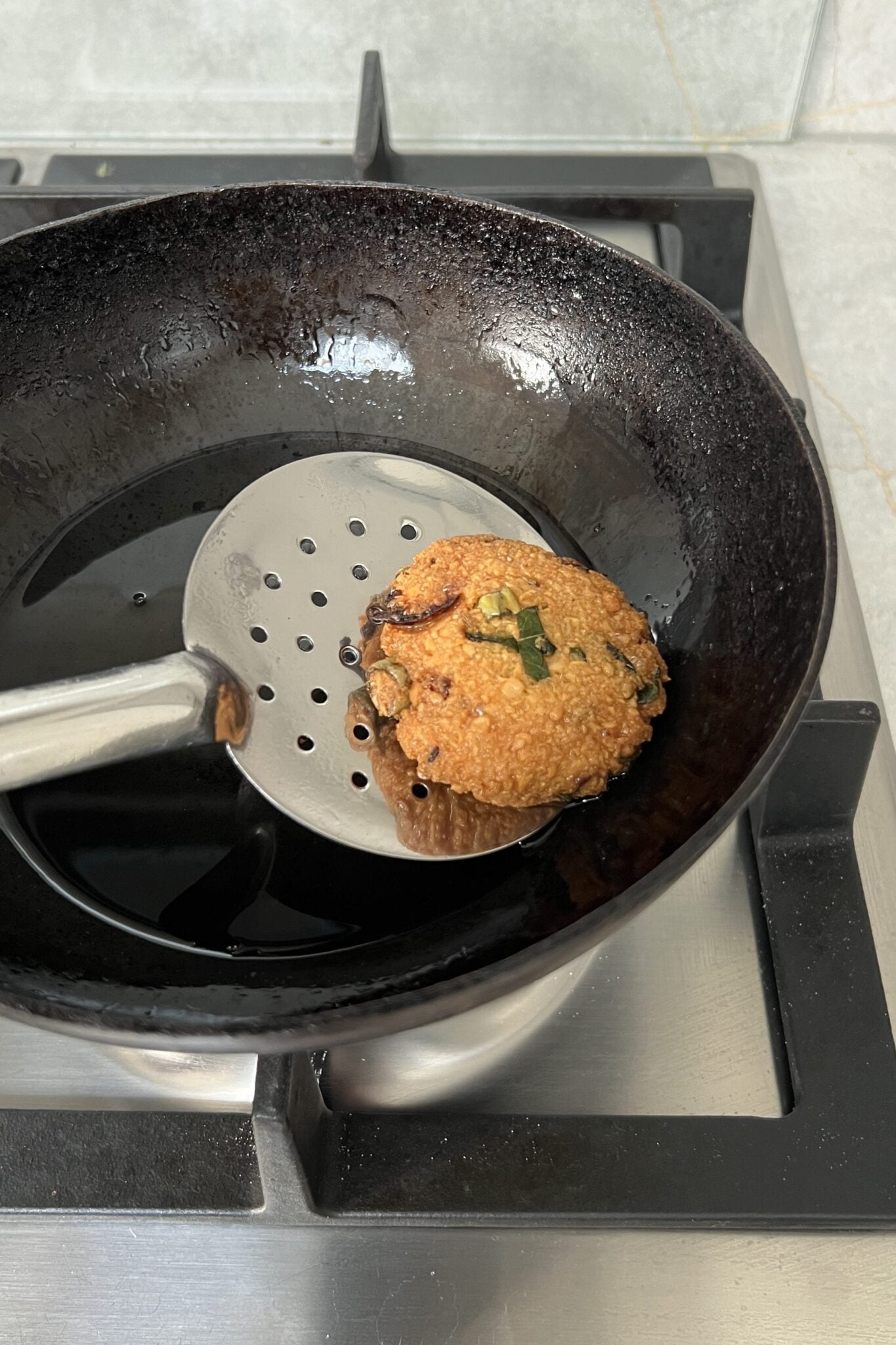 One deep fried chana dal vada on a slotted spoon.