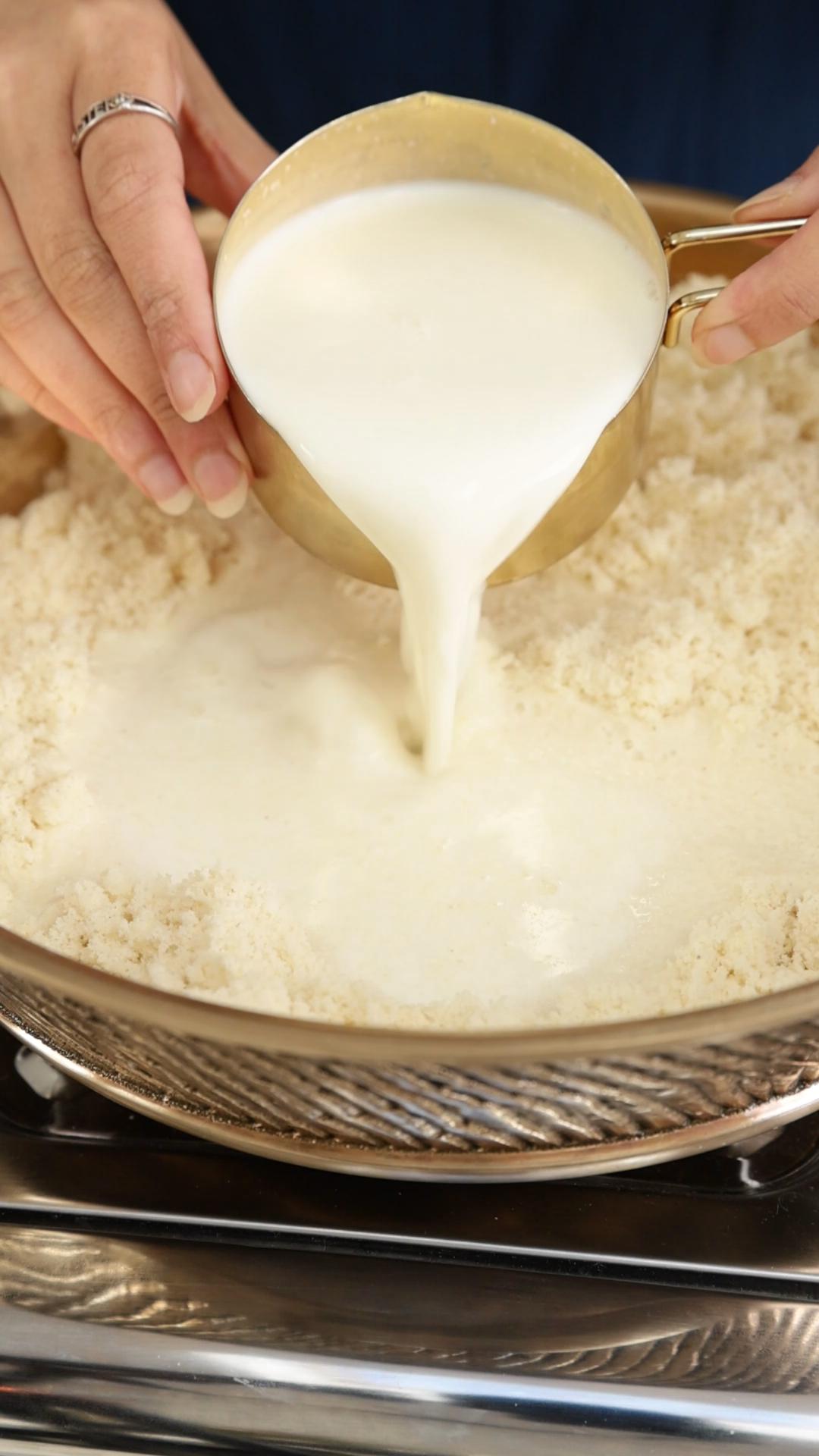 Female hand is pouring milk from the cup on roasted coconut and almond flour. 