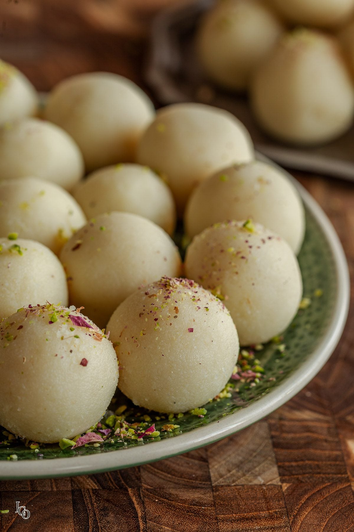 White coconut almond ladoos decorated with chopped pistachio nuts and dried rose petals. 