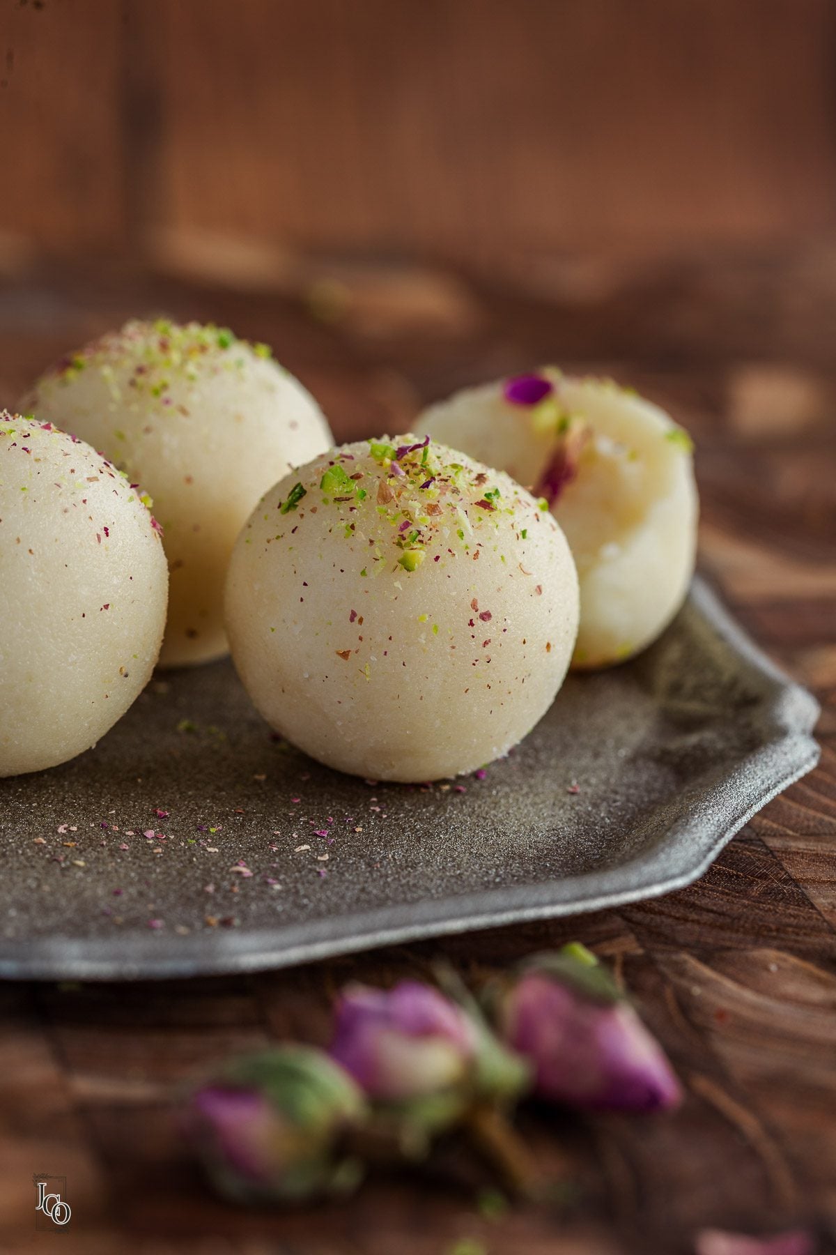 Three whole and one half cut coconut almond ladoo placed on a decorative tray. 