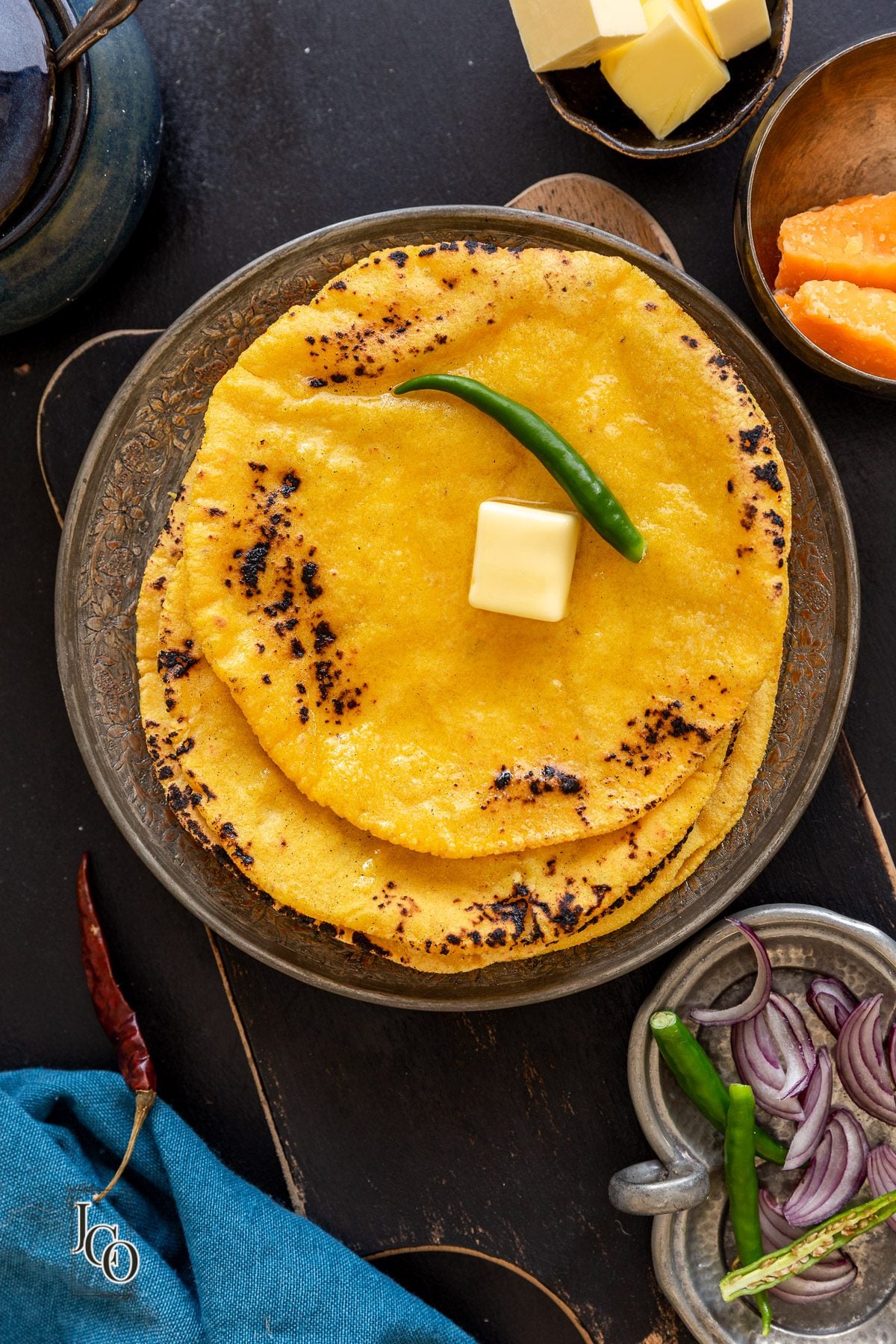 Makke di rotis on a plate, topped with a knob of butter and green chilli.