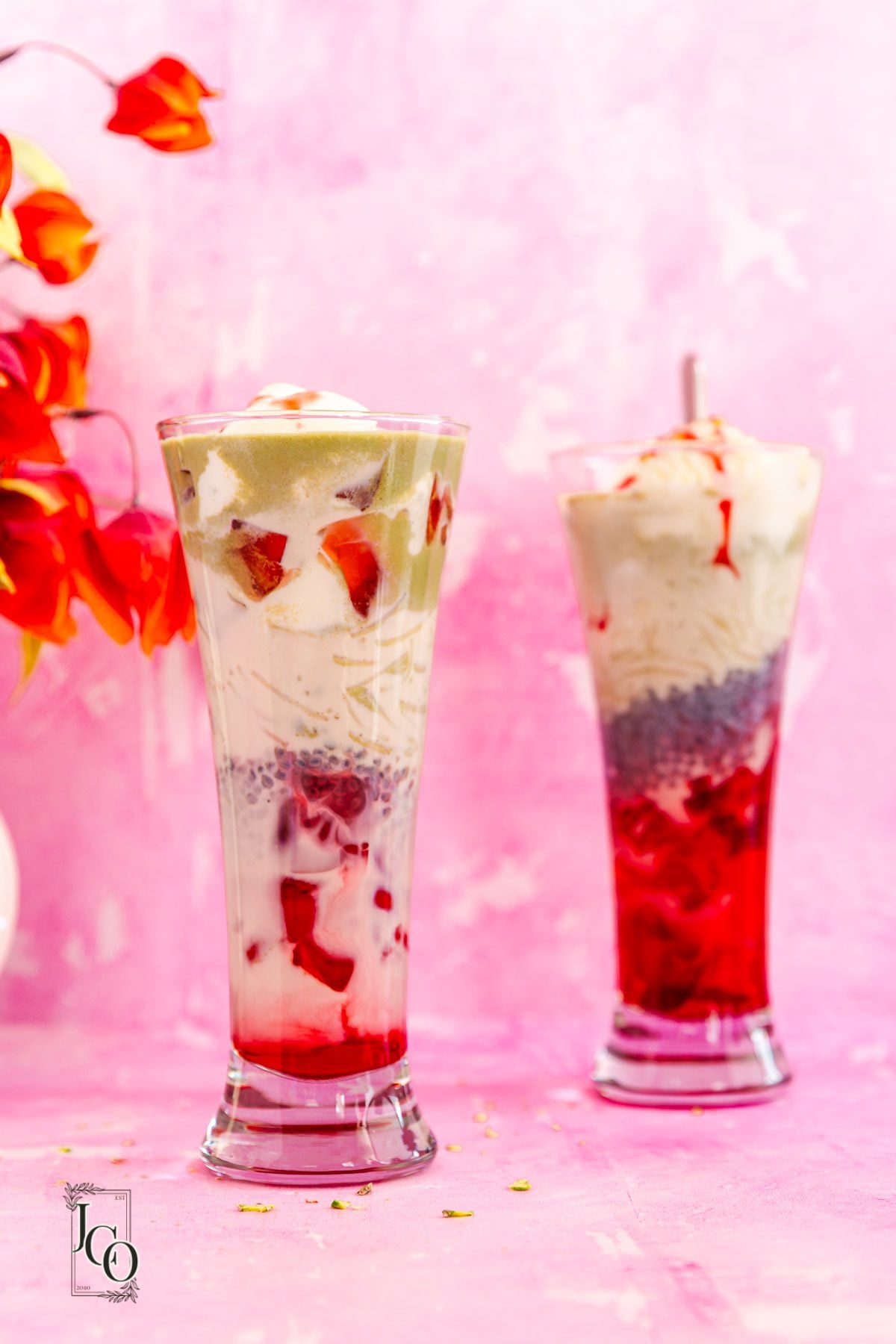 Two tall glasses of pistachio rose falooda placed near the flower vase on the table. 