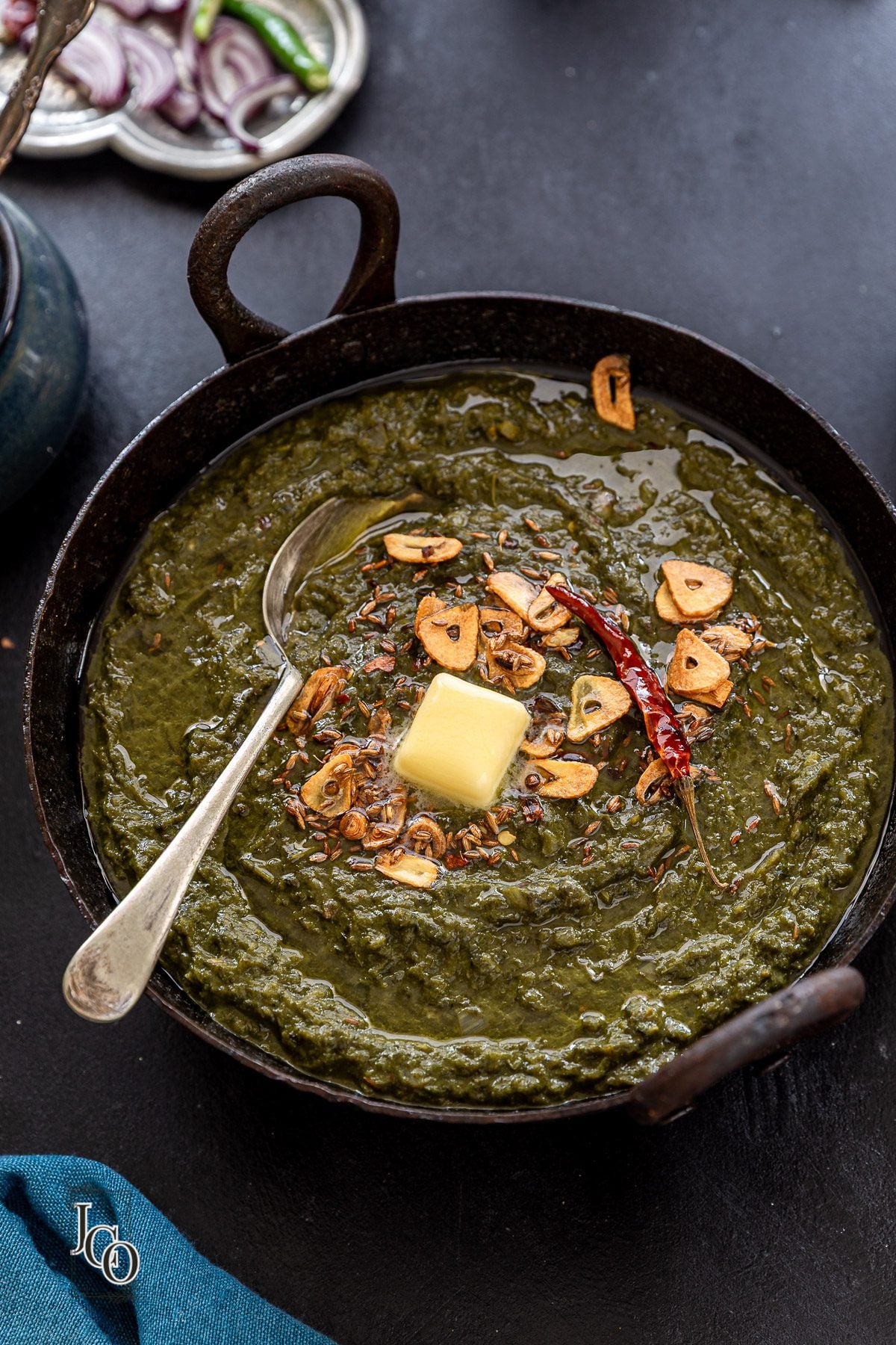 Sarso da saag in a iron kadai, served with a serving spoon.