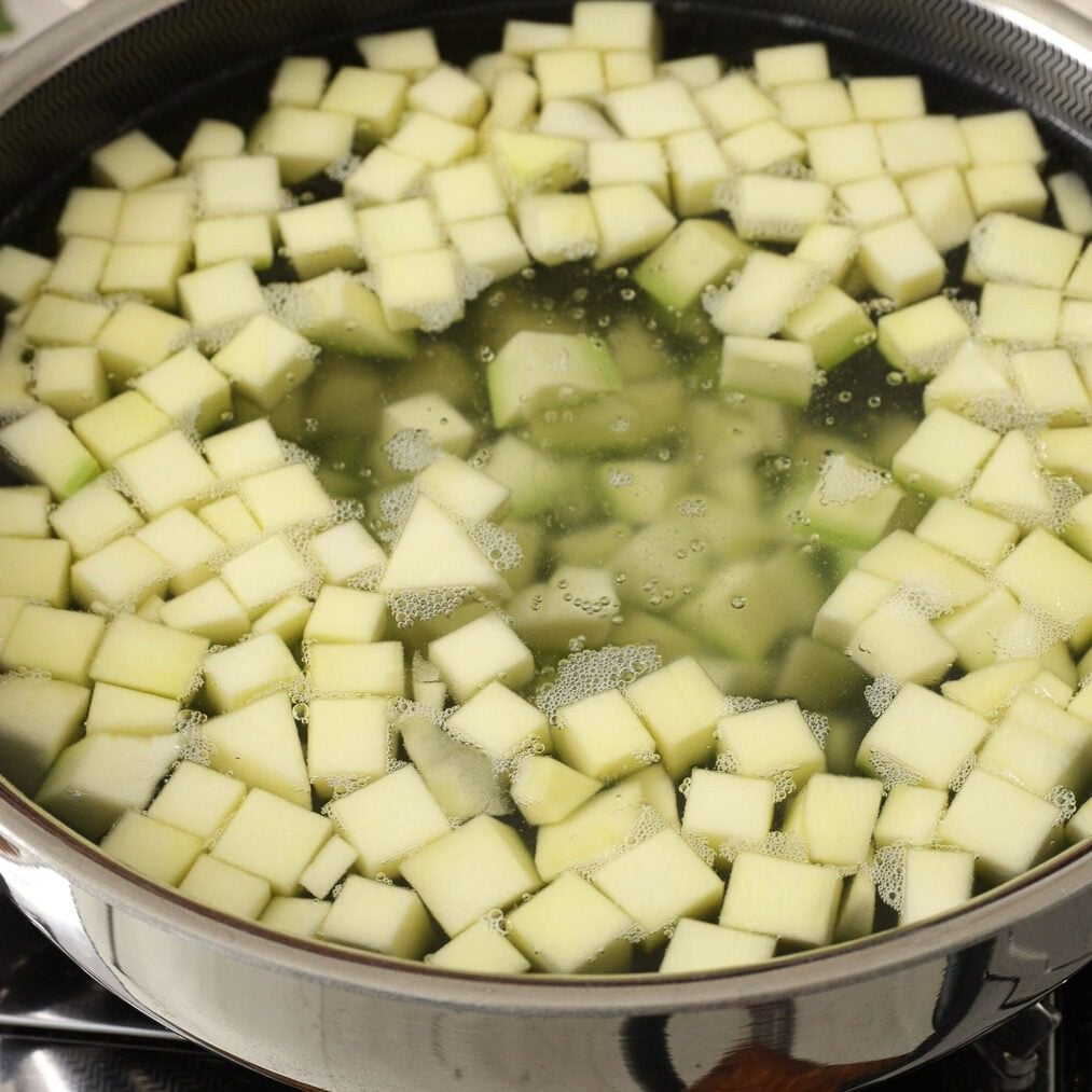Raw mango cubes boiling in hot water over the stove.