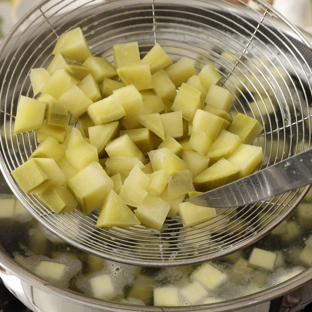 Boiled mango cubes in a strainer.