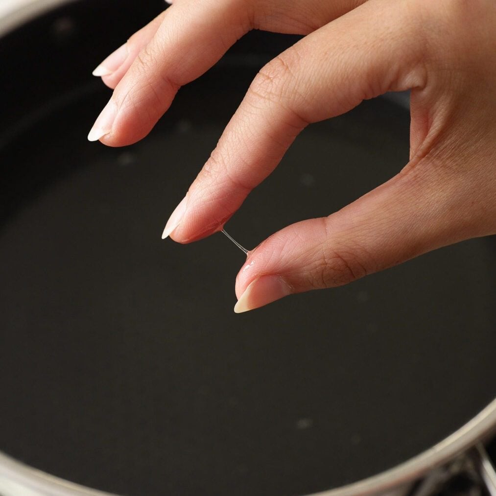 Female hand is showing one thread consistancy sugar syrup using her fingers.