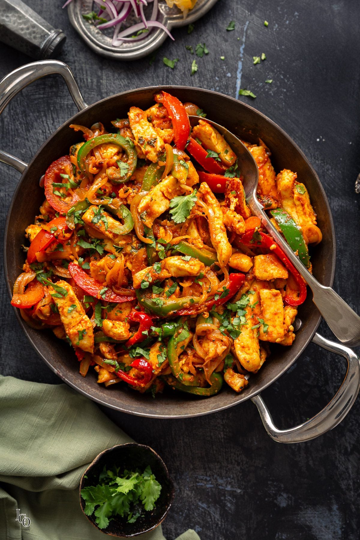 Paneer jalfrezi in a cast iron pan with a serving spoon. 