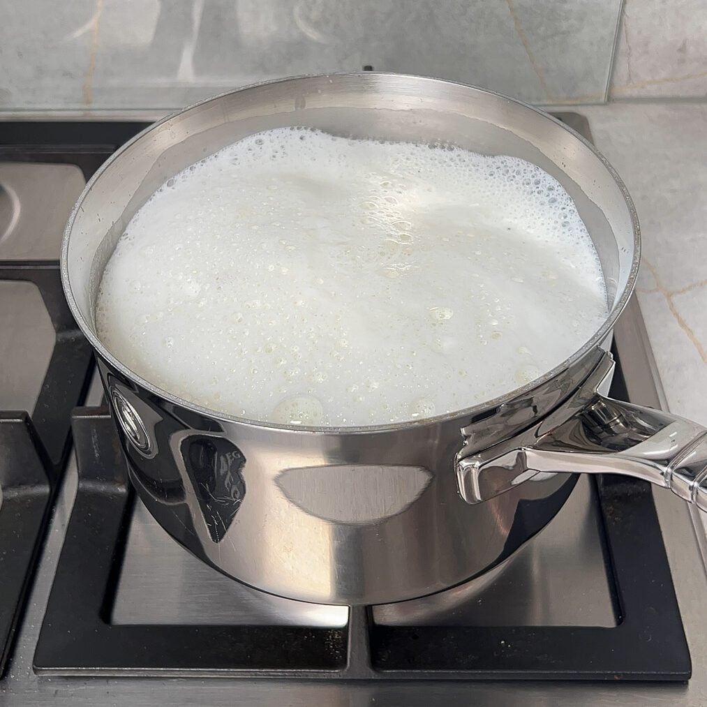 Milk boiling in a milk saucepan over the stovetop.