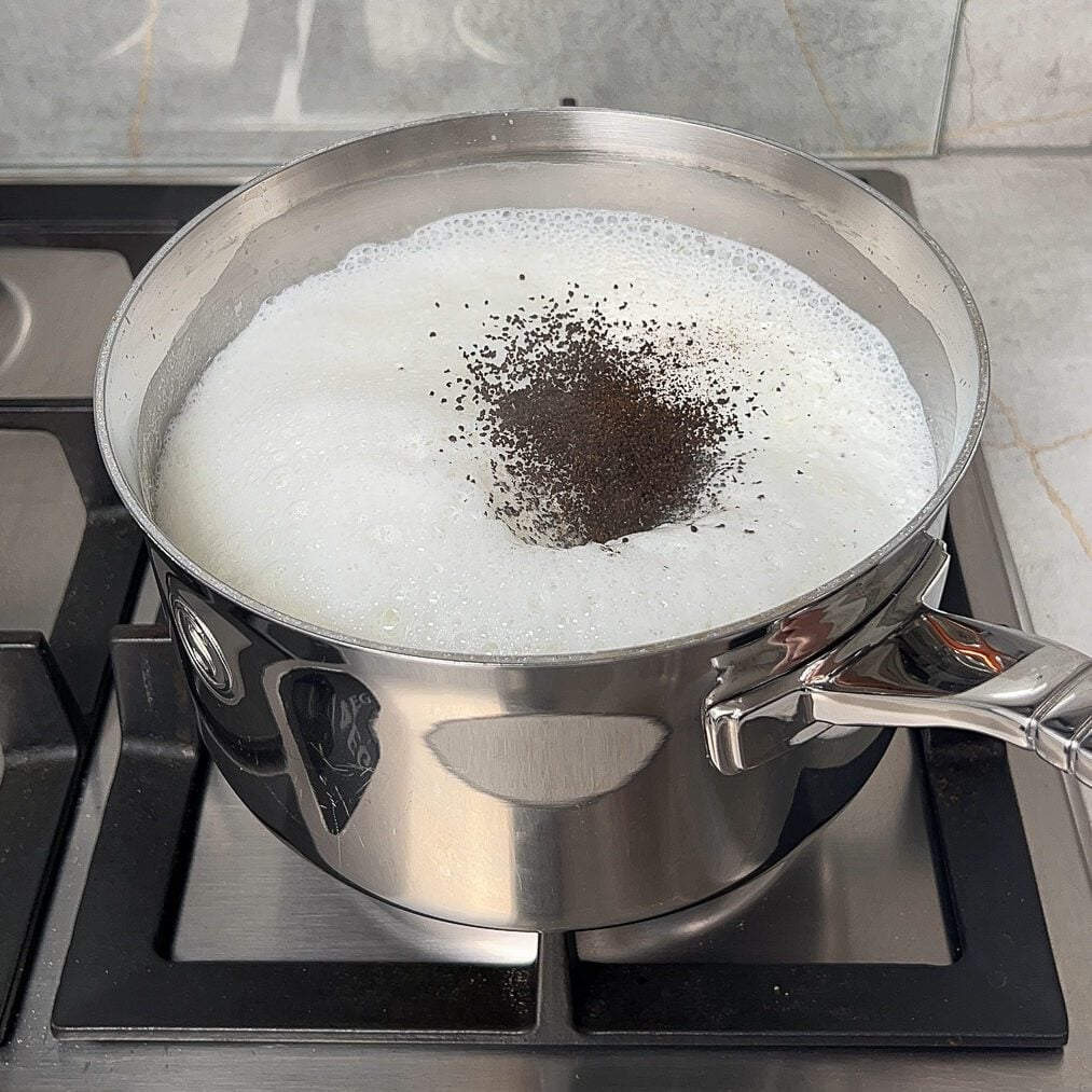 Loose black tea added to the boiled milk in a saucepan that is placed on the stove.