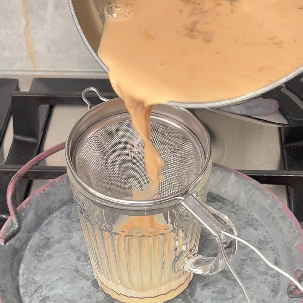 Chai being poured from the pan into clear glass through fine mesh seive.