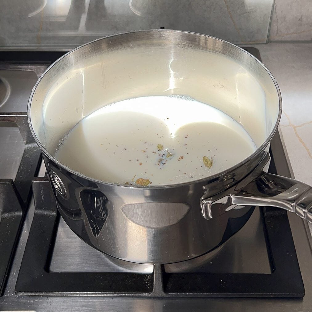 Milk and crushed cardamom in a milk saucepan on stovetop.
