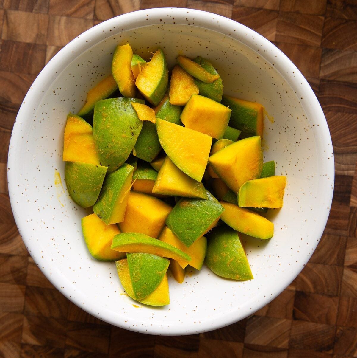 Cut raw green mango pickle pieces mixed with turmeric and salt in a bowl.
