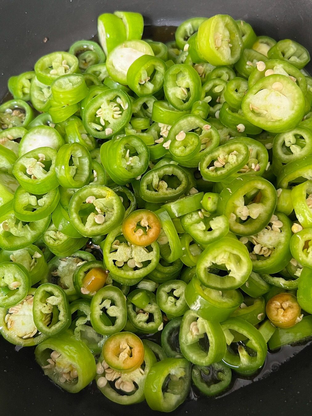 Sliced green chillies added to the mustard oil tempering in a black pan.