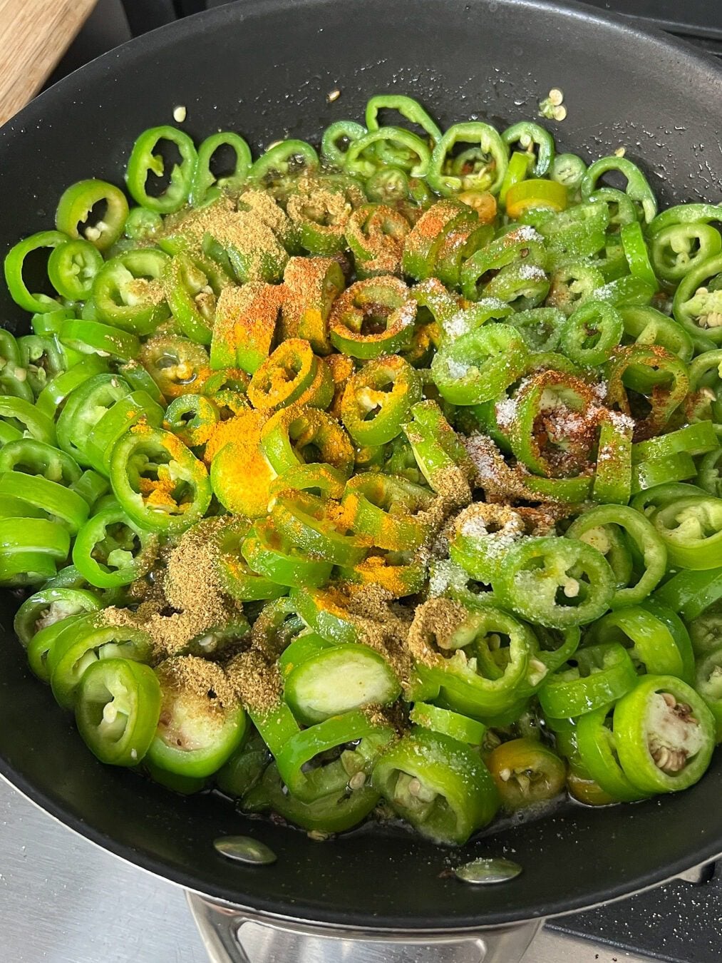 Spice powders added to the cut green chillies in a black pan.