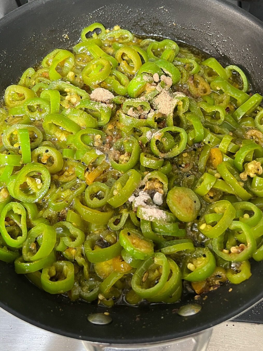 Salt and mango powder sprinkled on cooked green chilli pickle in a pan over the stove.