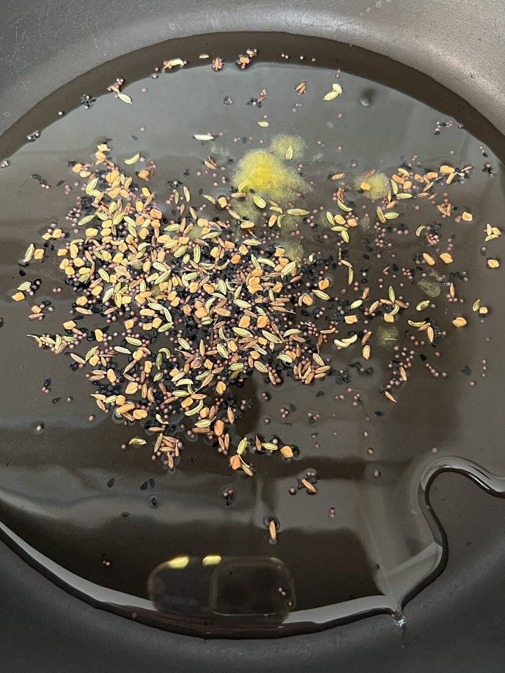 Indian five spices and yellow powder hing added to the hot mustard oil in a black pan.