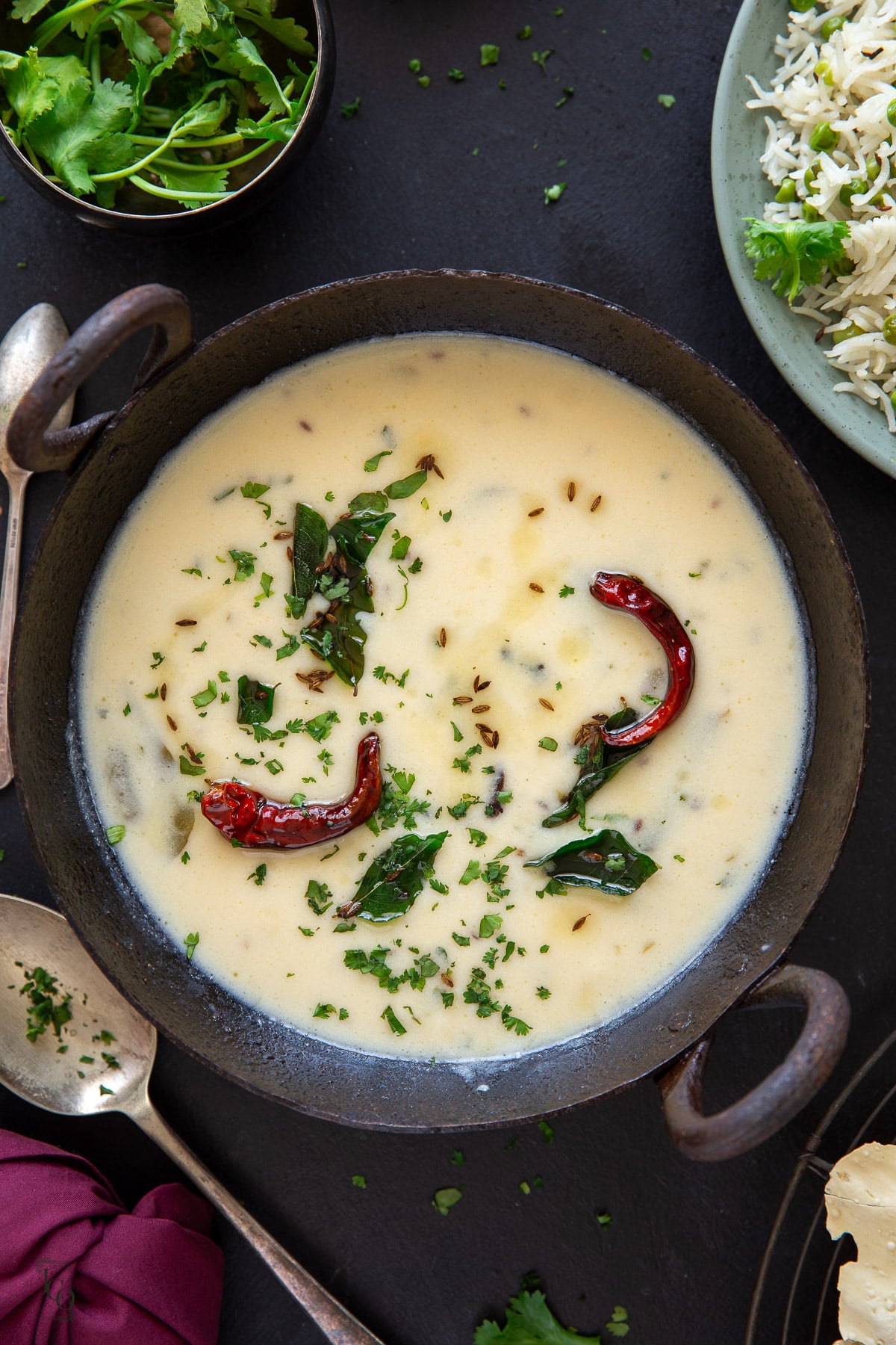 White kadhi with curry leaves and dried red chillies in a serving kadai bowl. 
