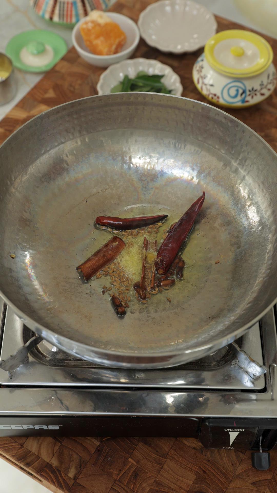 Ghee tempering in a pan with dried red chillies, cloves, cinnamon and cumin seeds. 