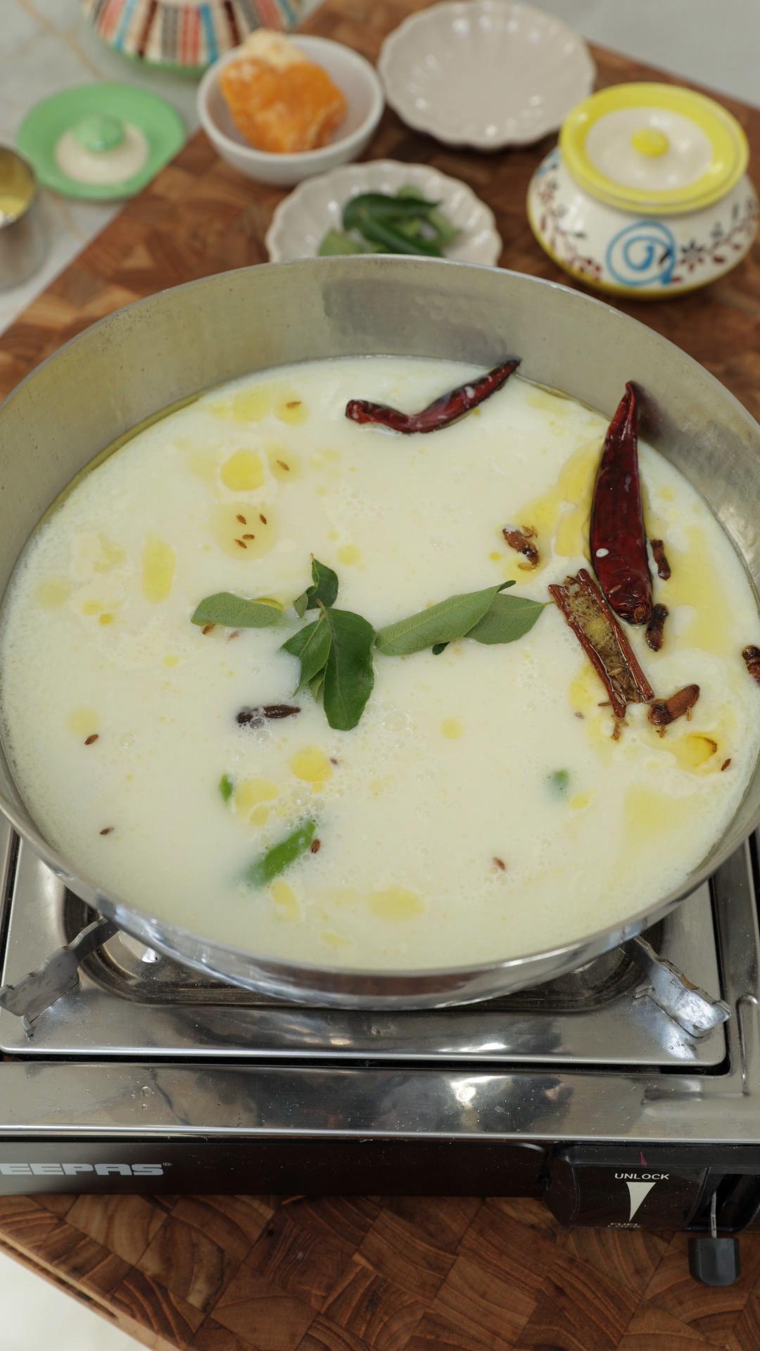 Thinned yogurt and besan mixture and curry leaves in a pan. 