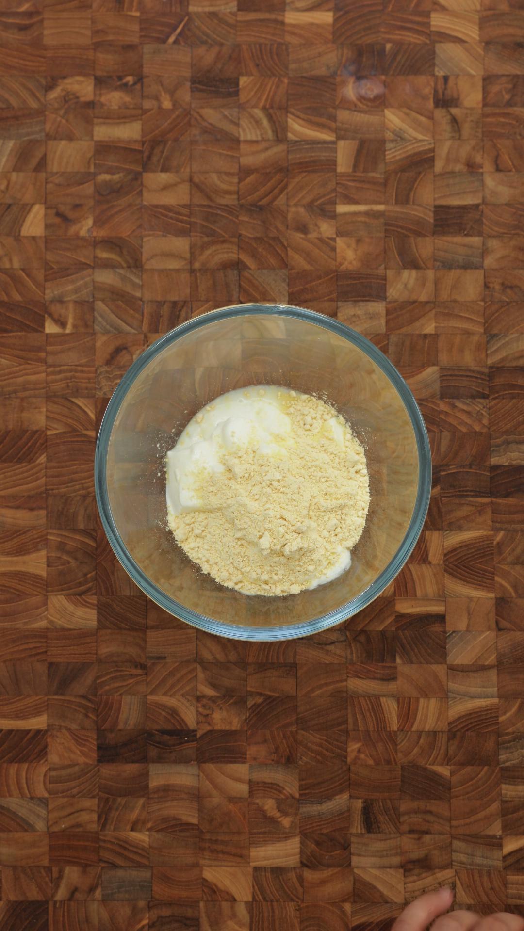 Plain yogurt and chickpea flour in a clear glass bowl.