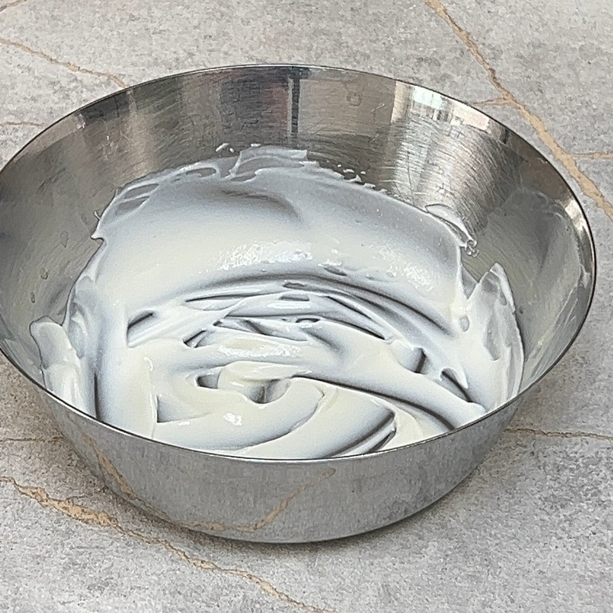 Whisked plain yogurt in a stainless steel bowl.