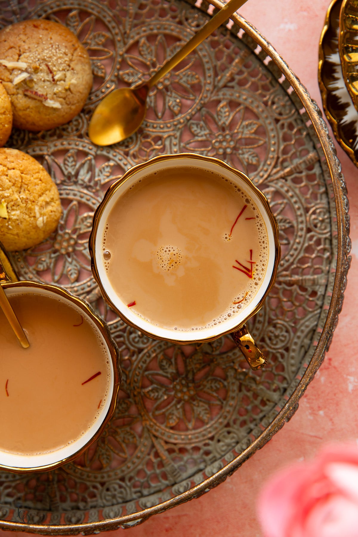 Two cups of indian chai garnished with saffron strands placed on a decorative tray.