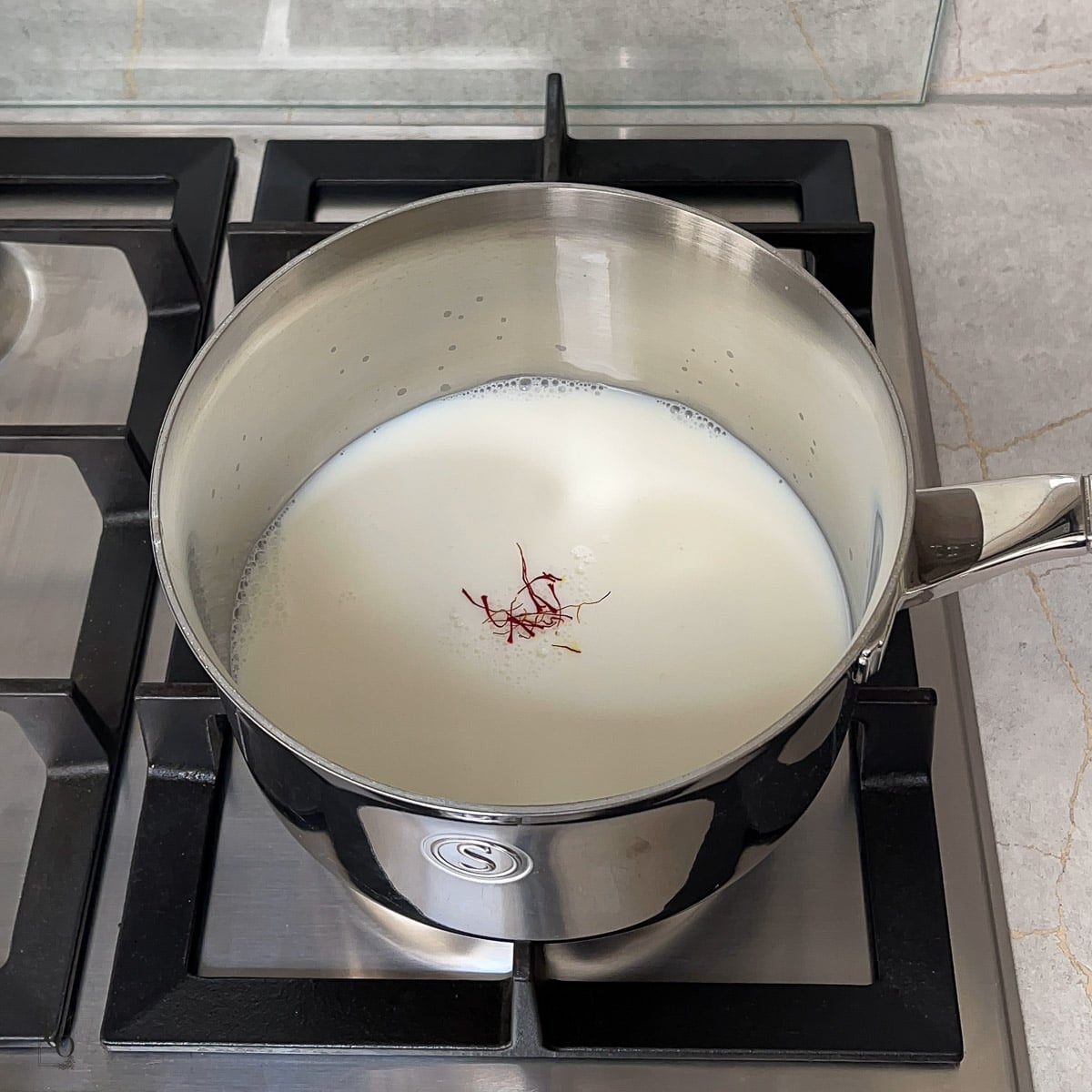 Milk and saffron strands in a milk pan on the stovetop.