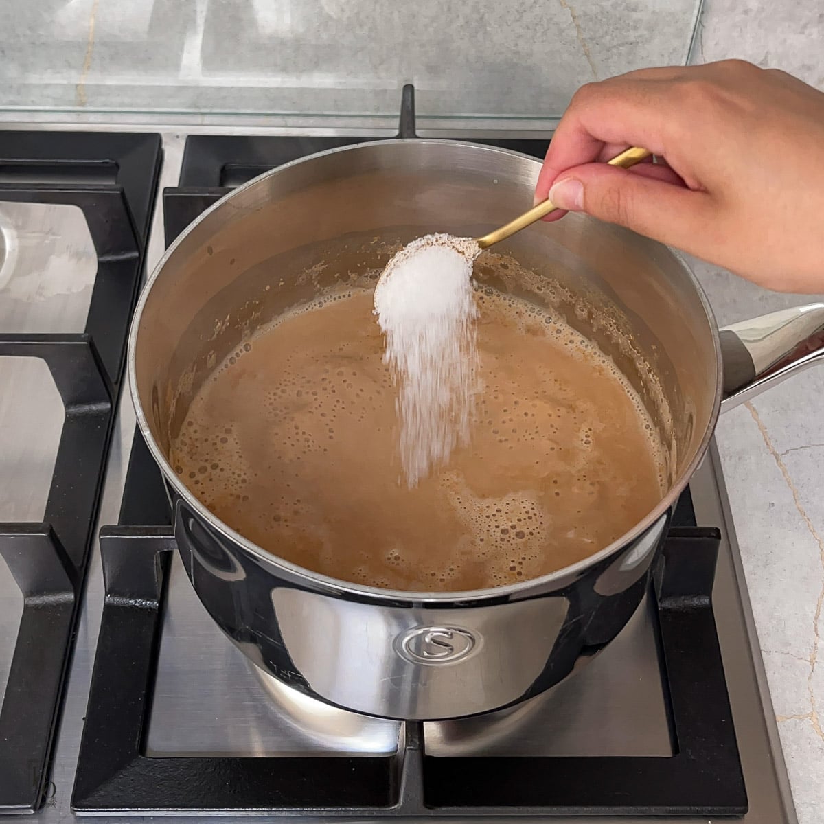 Sugar being added to tea in a pan.