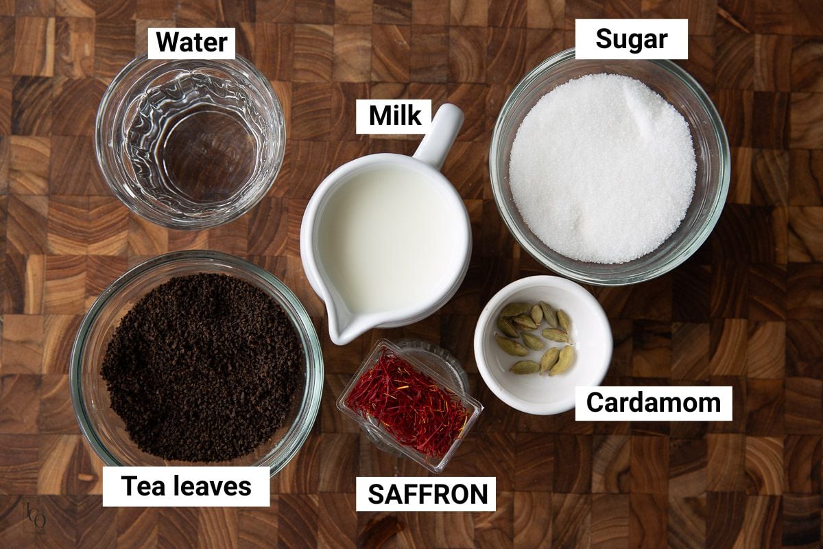 Milk, loose tea leaves, saffron, sugar, water and cardamom pods in bowls.