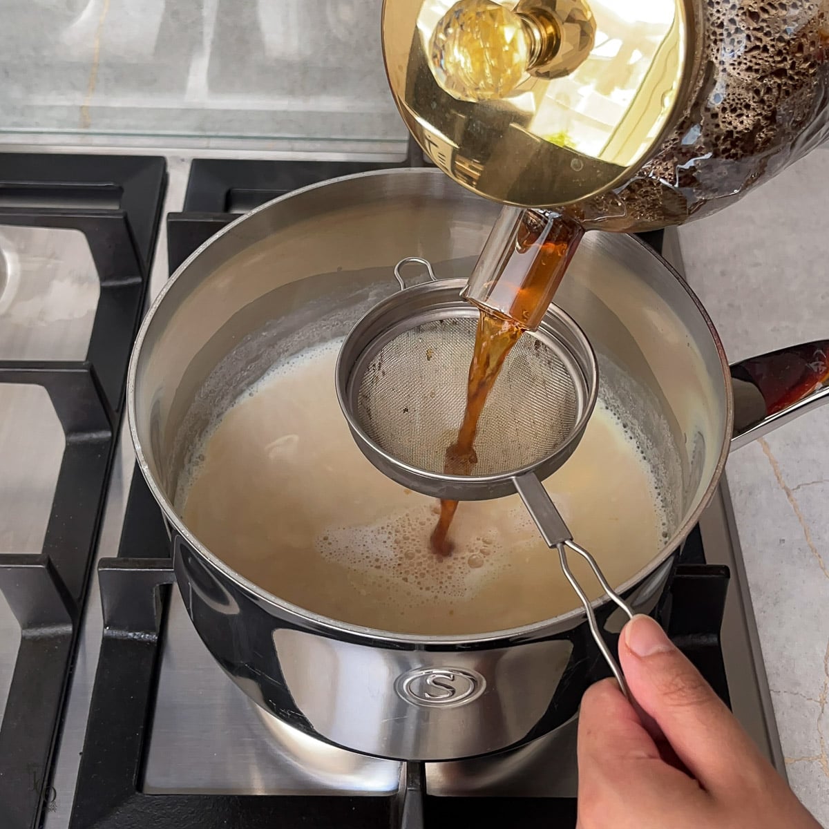 Brewed black tea being poured in saffron infused milk.