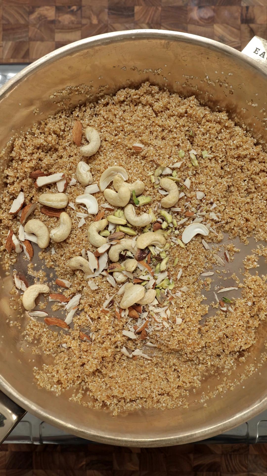Mixed nuts added to ghee roasted broken wheat in a pan.