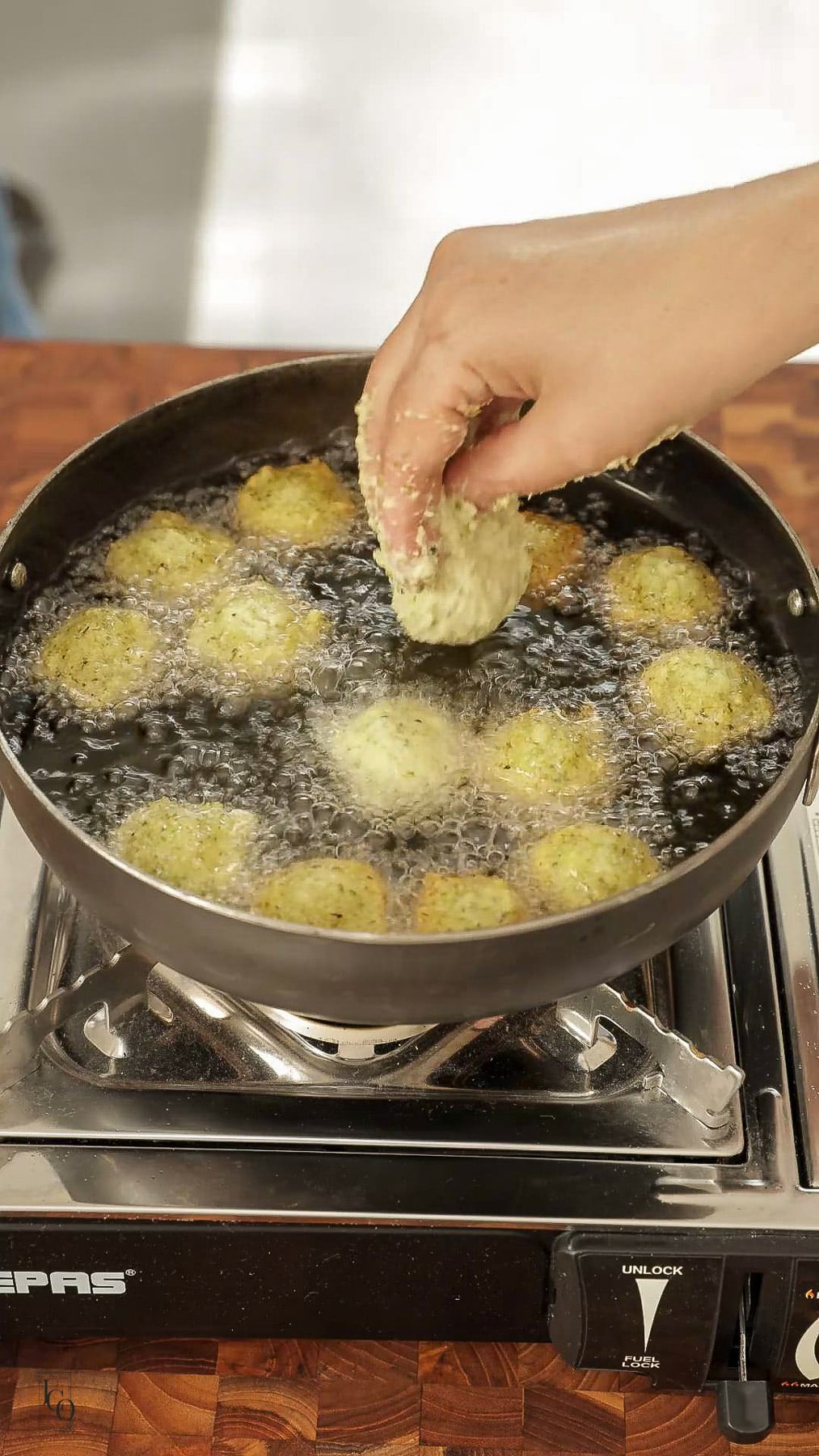 Female hand is dropping a small amount of batter in hot oil.