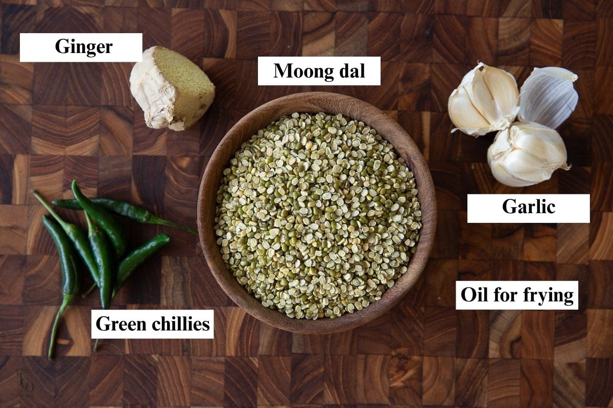 Split green moong dal, garlic, ginger and green chillies on brown surface. 