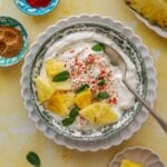 Pineapple raita topped with pineapple pieces, sprinkled red chill powder and chaat masala.