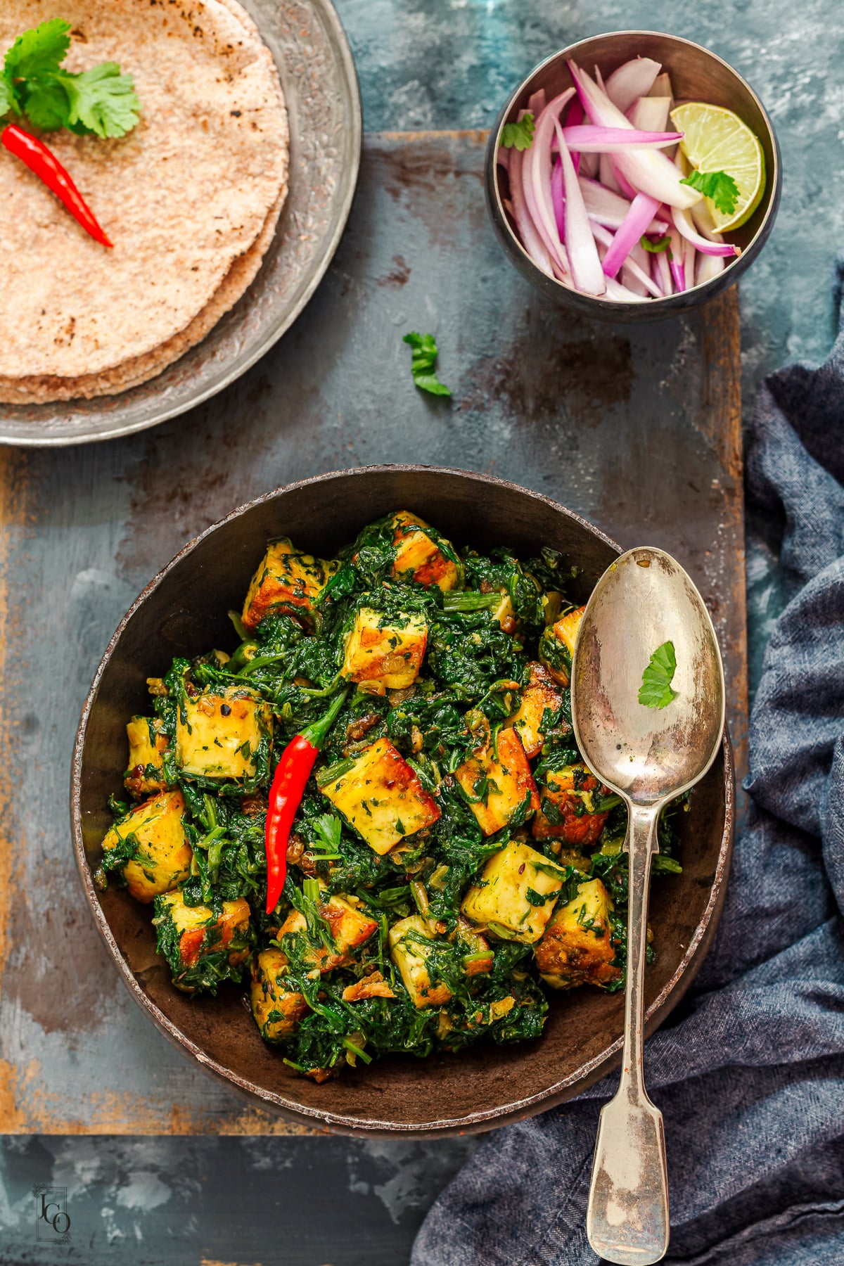 Indian spinach paneer curry served with roti and indian onion salad in a bowl.