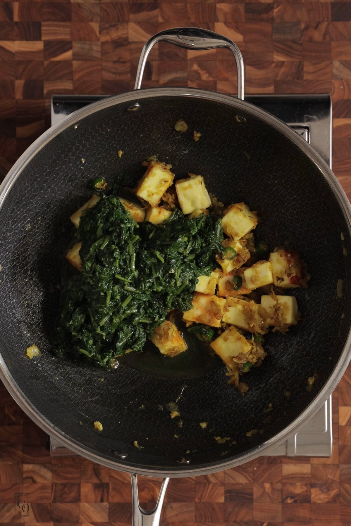Cooked spinach and sauteed paneer added to the spicy onion masala in a pan.
