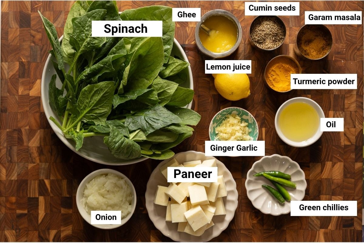 Fresh spinach, paneer, spices, onion, ghee and oil in bowls.