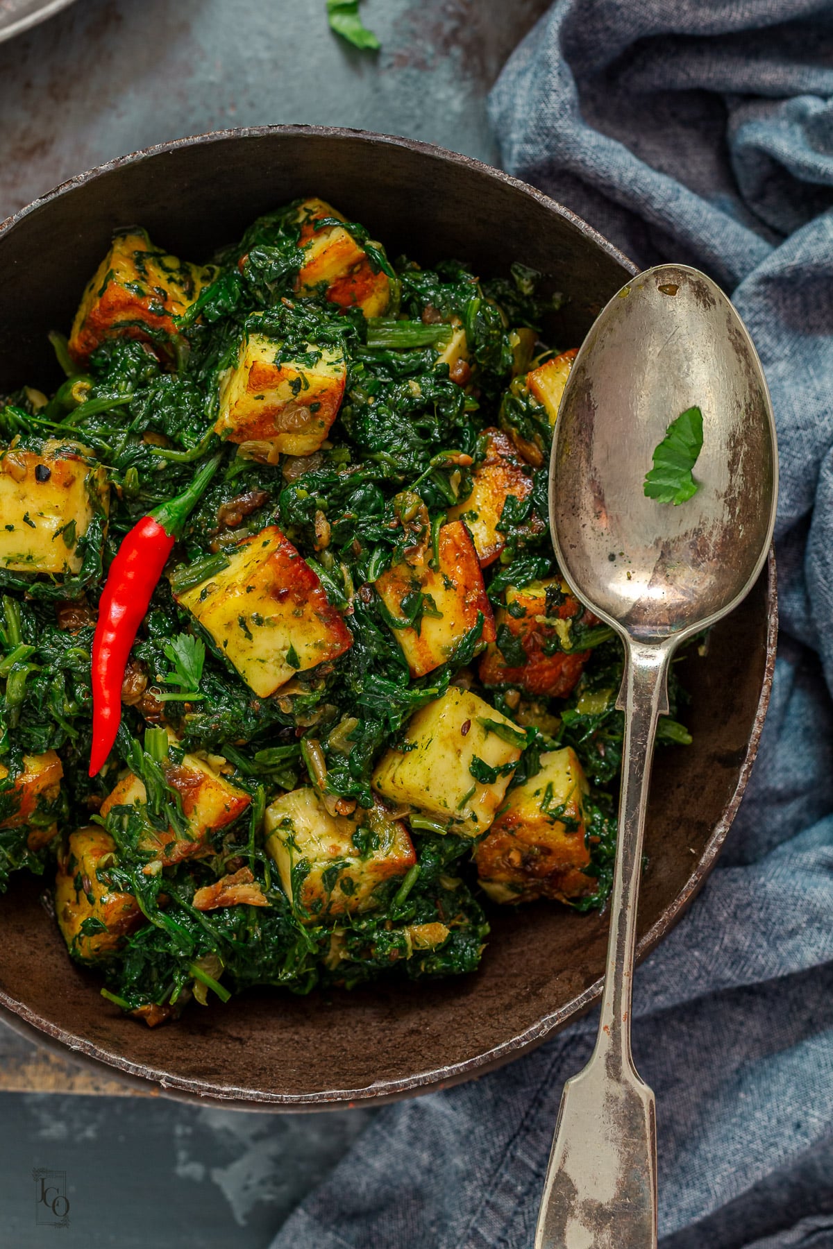 Paneer in coarsed spinach served in a metal bowl.