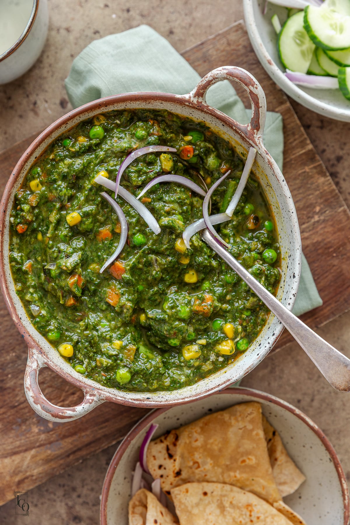 Vegetable palak curry garnished with thin sliced red onions and served with roti.