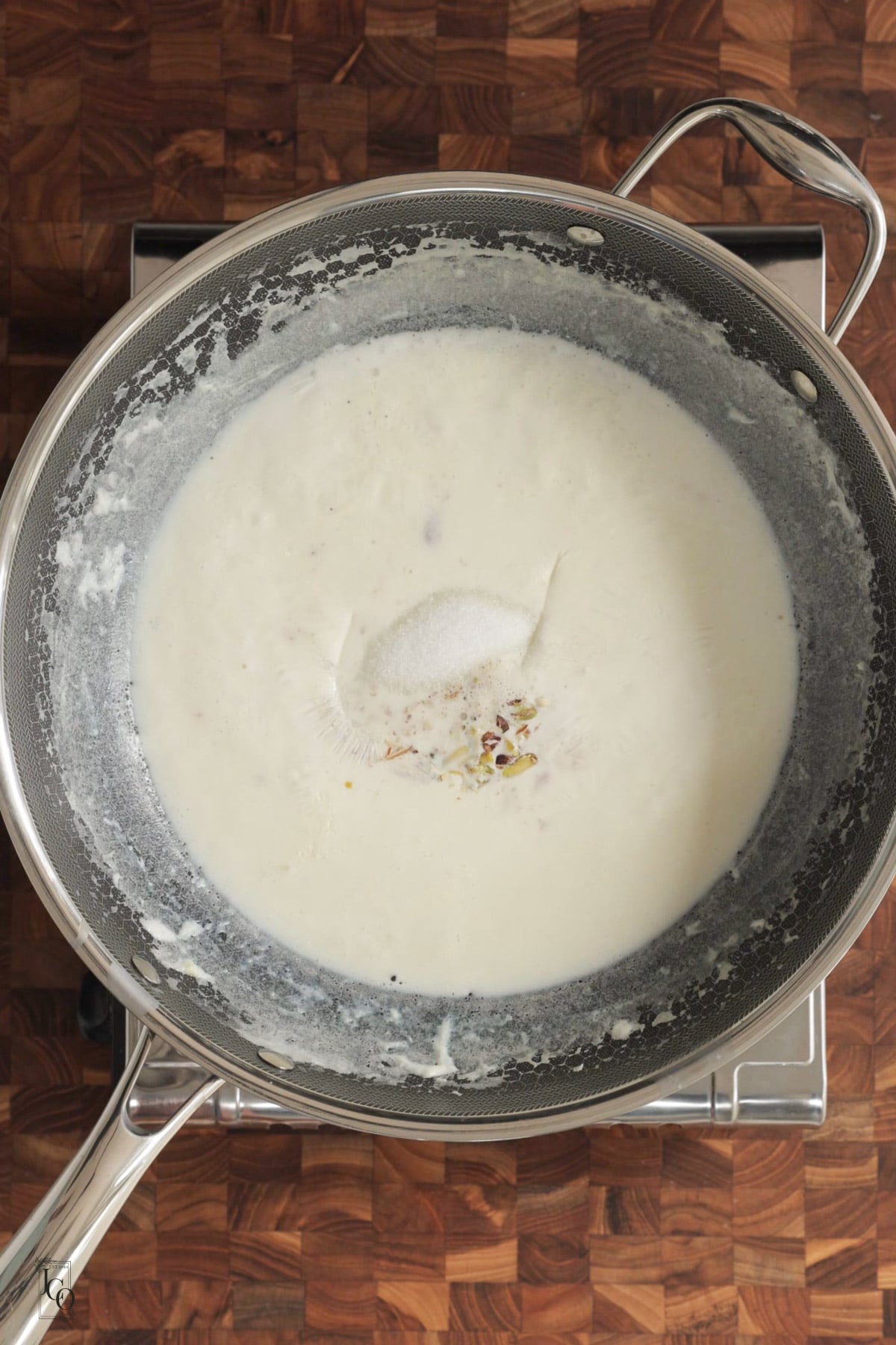 Sugar, chopped nuts and cardamom powder added to the thickened milk in a pan.