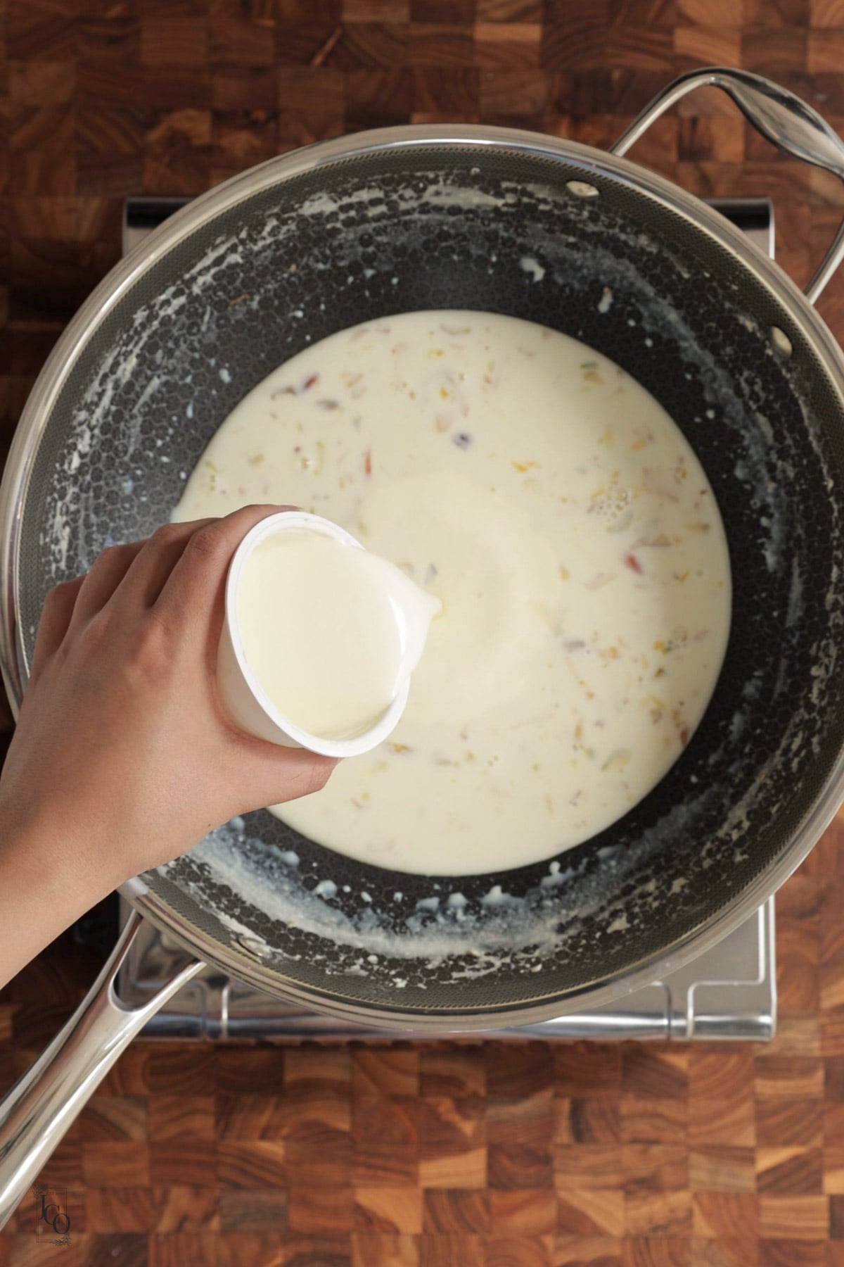A female hand is pouring cream in thick milk mixture.