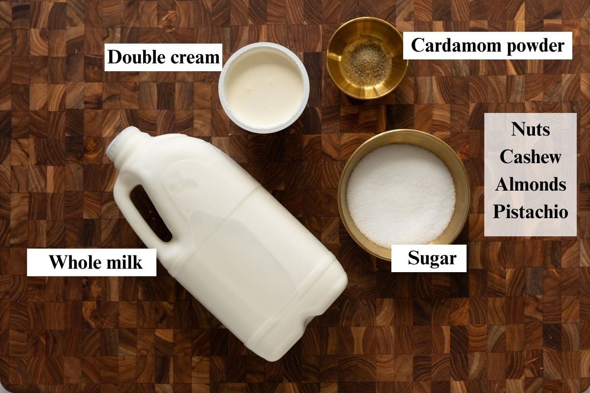 Whole milk carton, cream, sugar and cardamom powder in bowls on brown surface.