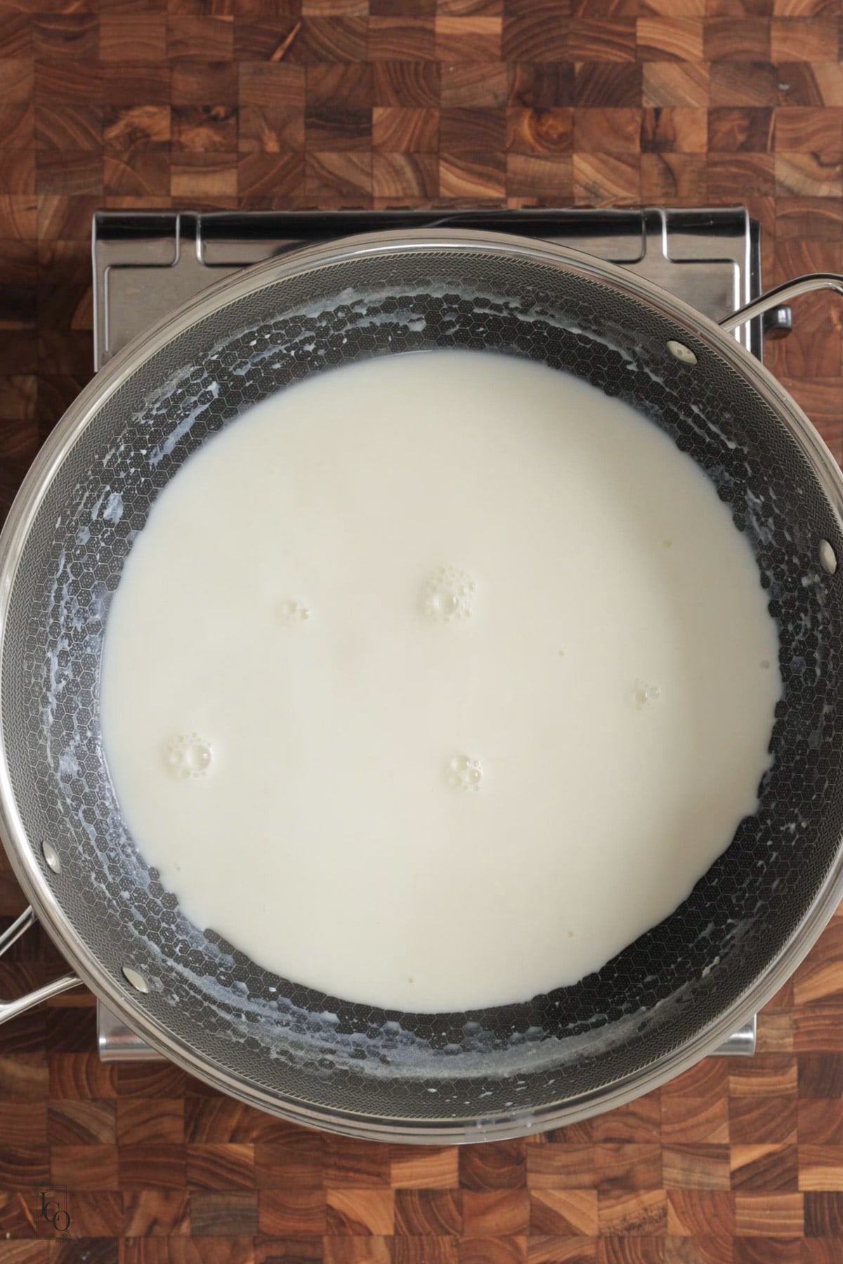 Whole milk boiling in a wide mouth pan on the stove.
