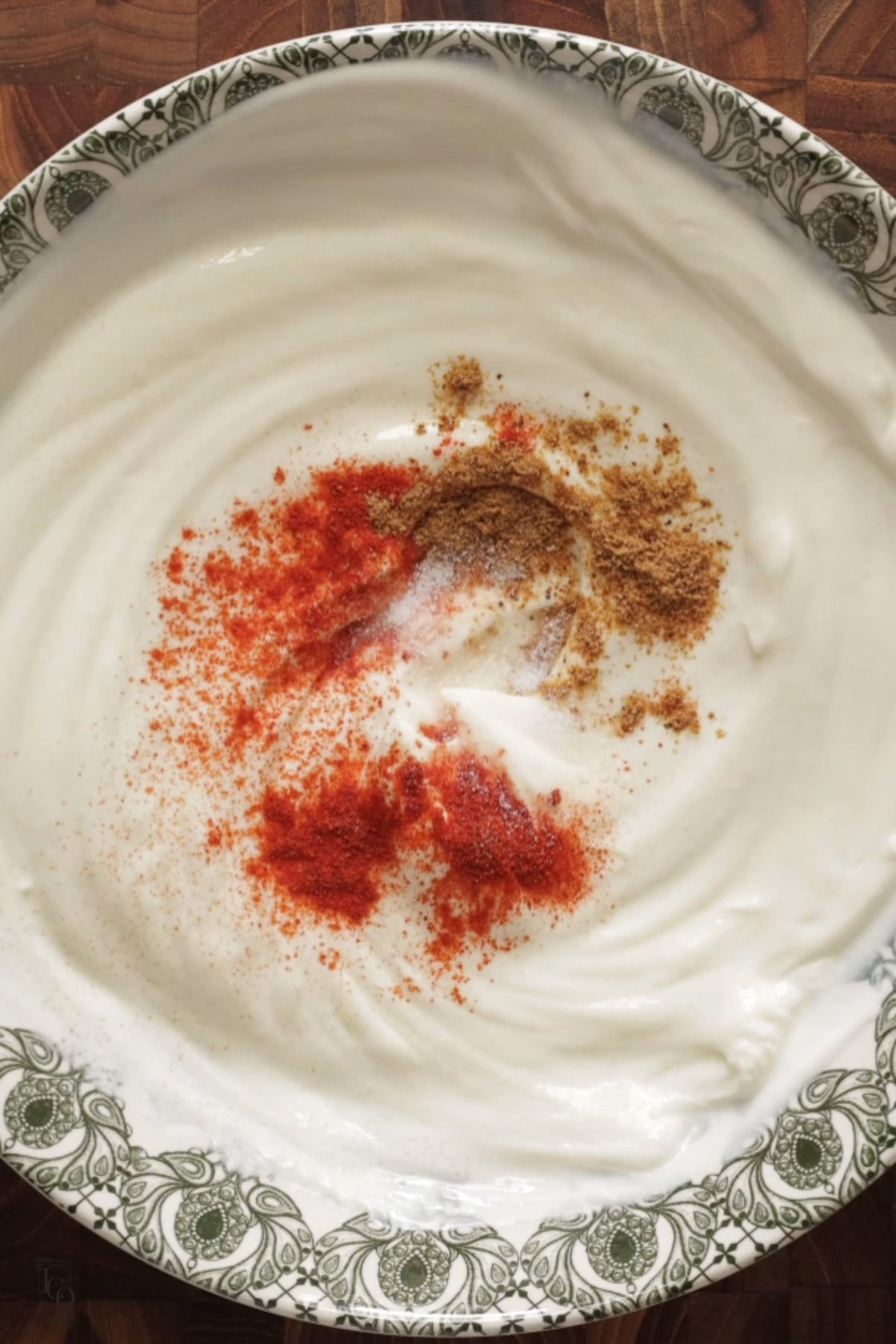 Red chilli powder and chaat masala added to the whisked plain yogurt in a bowl.