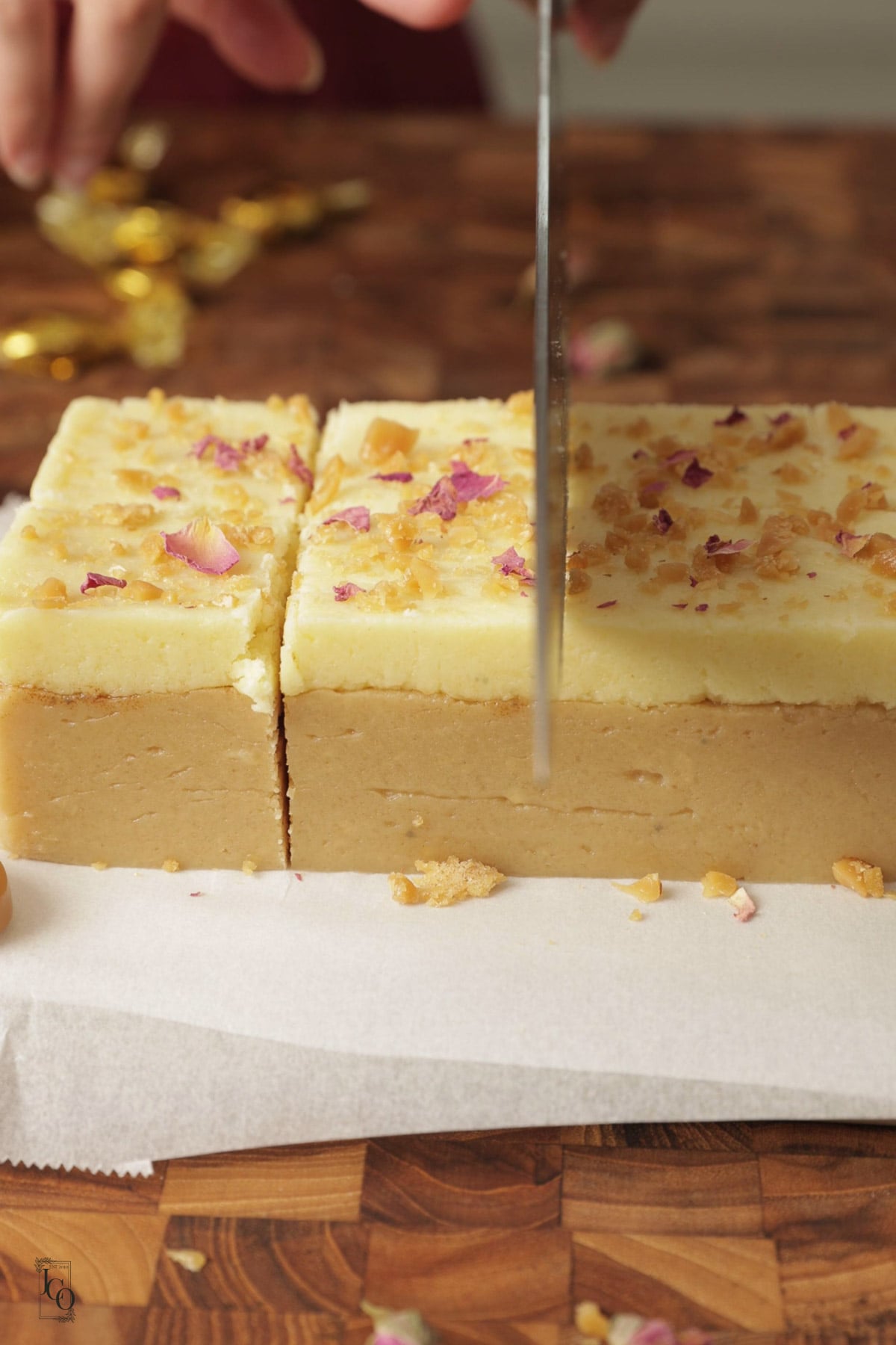 Female hand is cutting barfi into squares using a knife. 